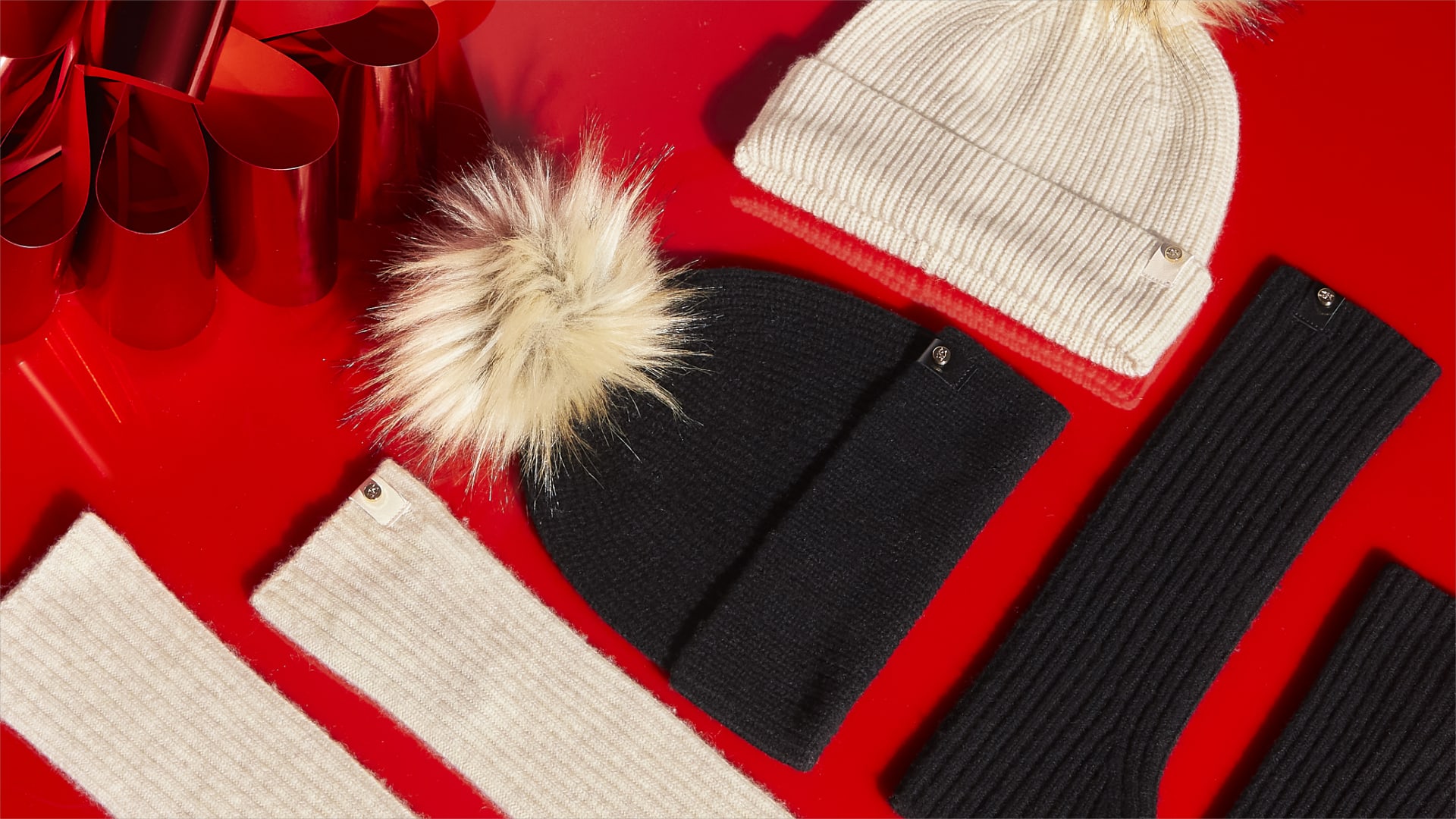 Black and beige knitted hats with fluffy pom pom and matching fingerless gloves displayed with red ribbon