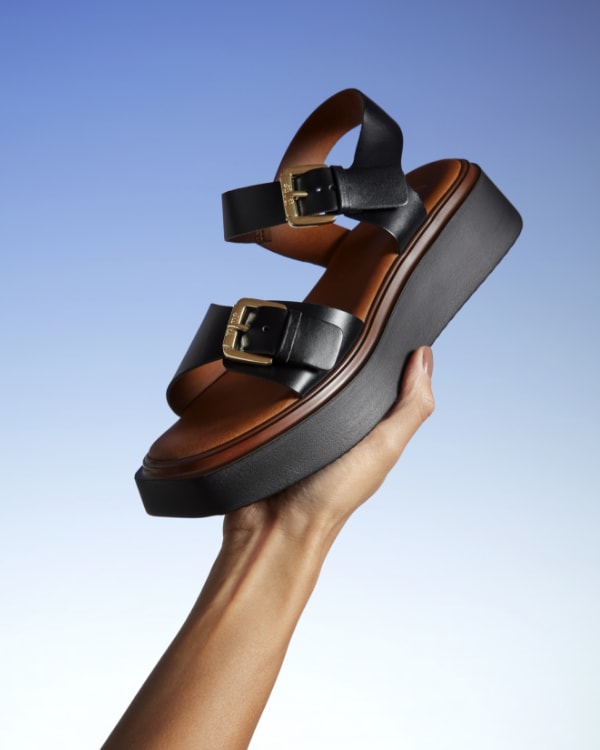 Hand holding a chunky black sandal with a flatform sole and large buckle detil