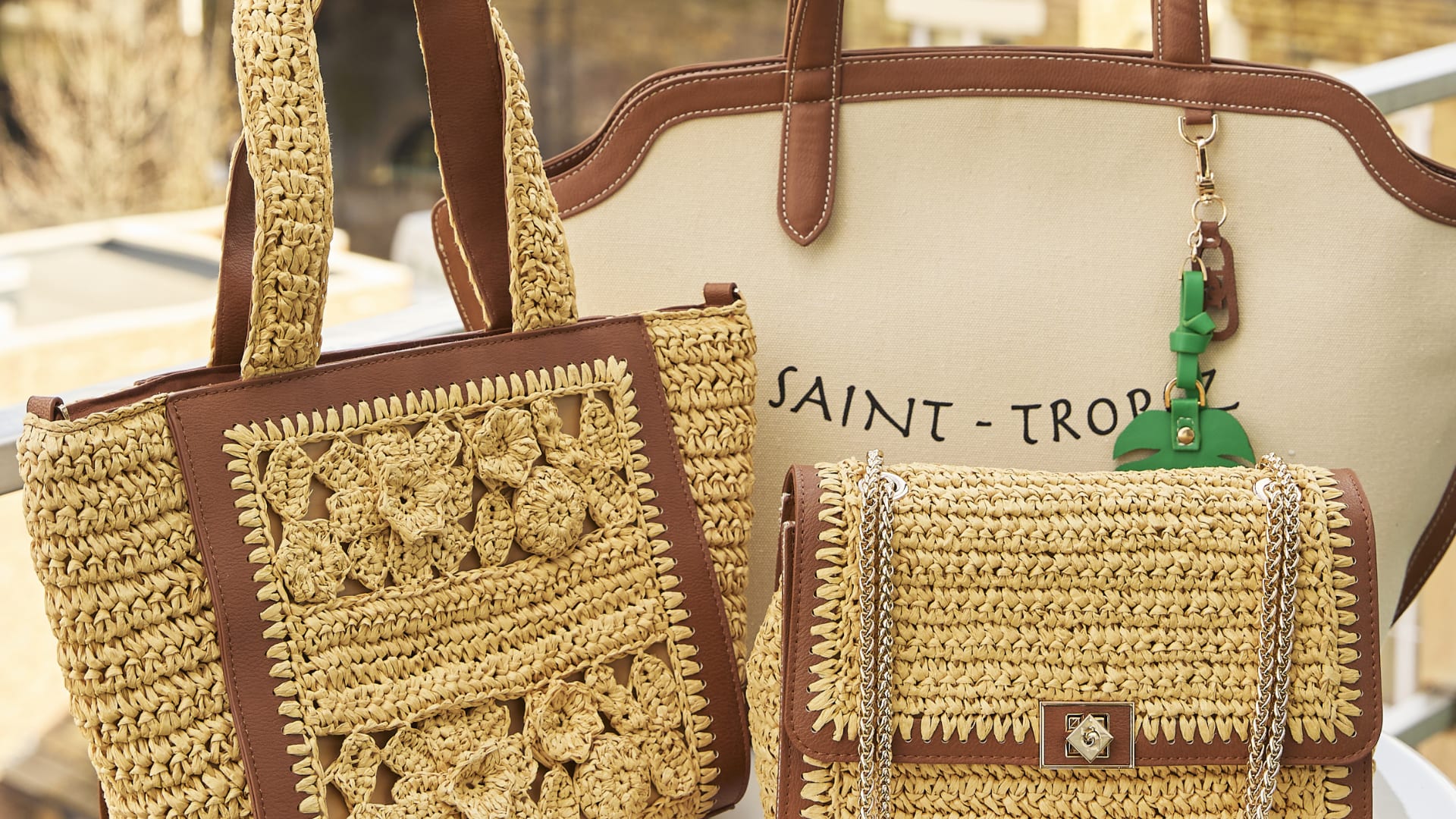 Natural raffia bags with different features, woven detail, chain strap and a slogan.