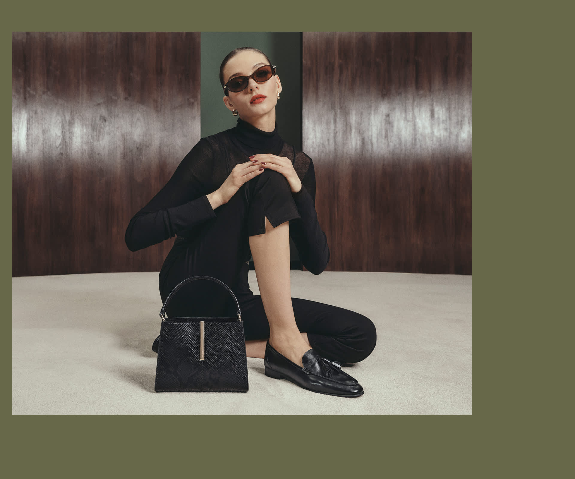 A woman sat on the floor wearing loafers with a dune london bag next to her 