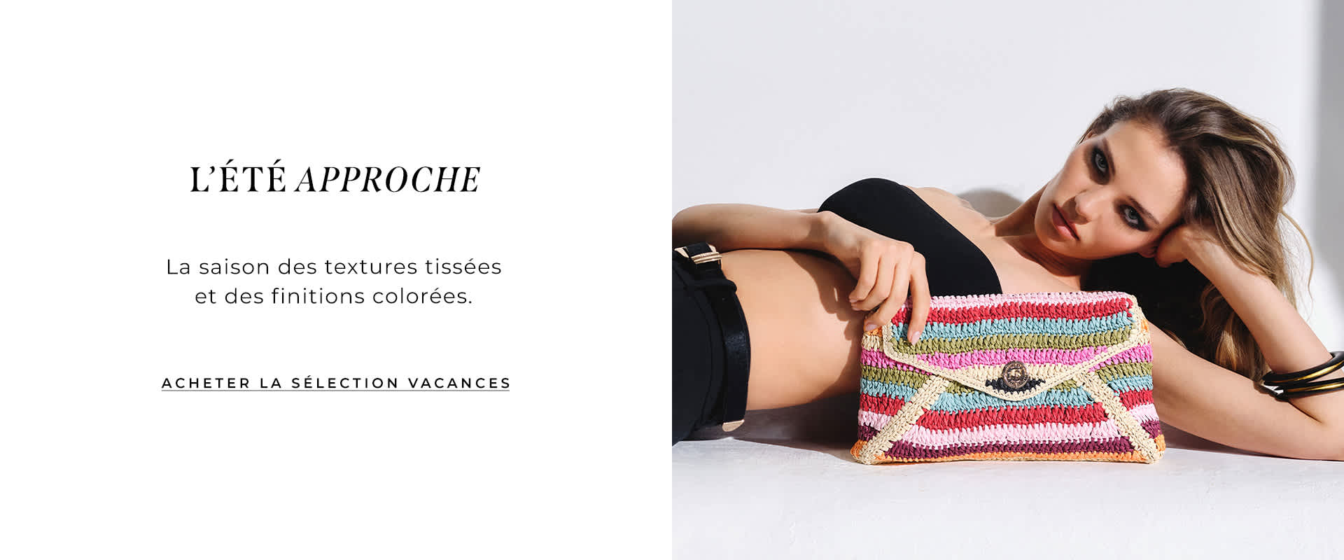 model laying down holding the essentials multicoloured stripe raffia clutch bag
