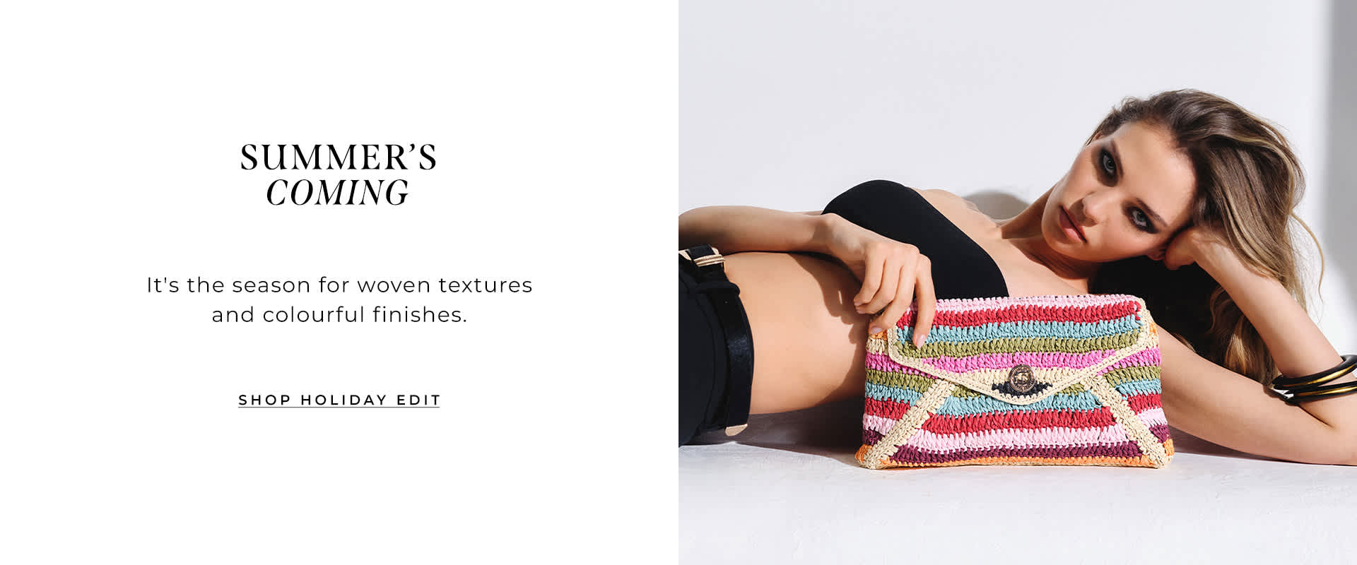 model laying down holding the essentials multicoloured stripe raffia clutch bag